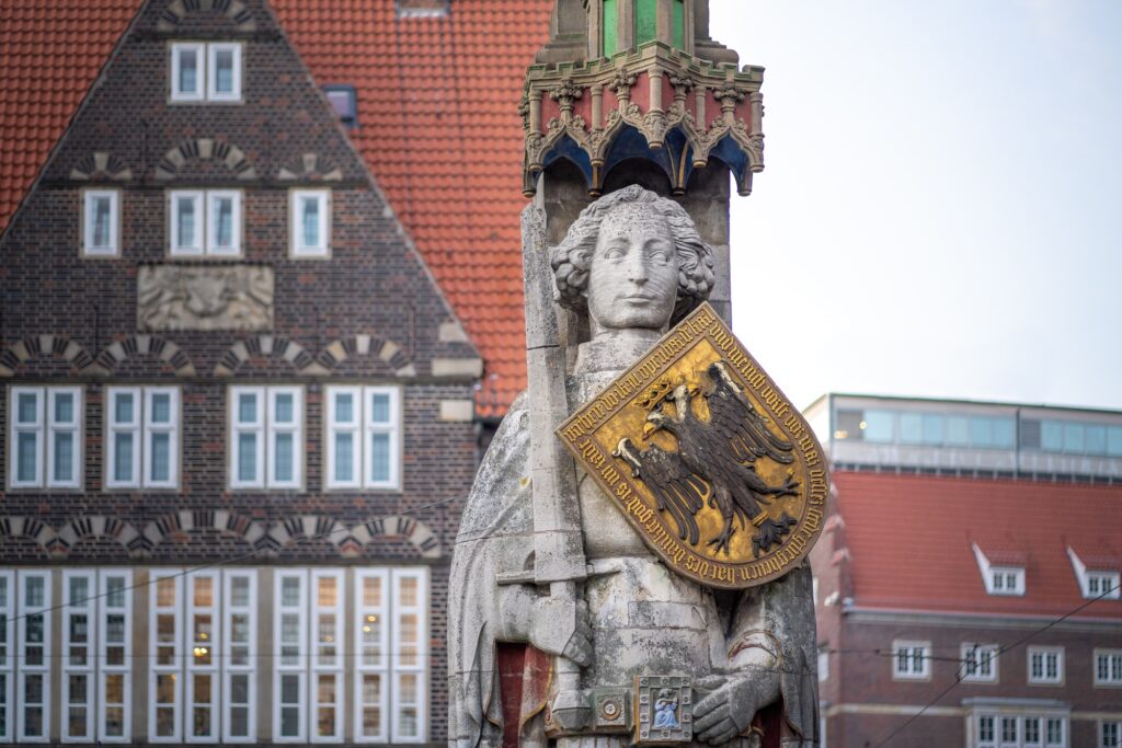 Steinfigur mit Schild und Adler vor historischem Backsteingebäude - Symbol für Würde und Vertrauen bei YANA Bestattung.