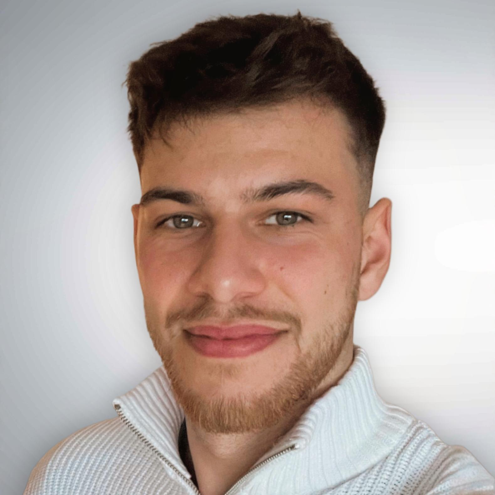 Junger Mann mit kurzem Haar und Bart, lächelt freundlich vor hellem Hintergrund - Symbolbild für günstige Bestattungen.