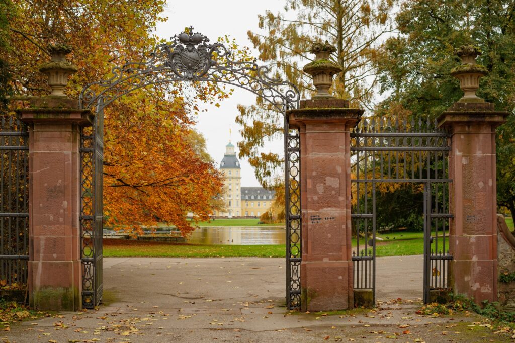 Eingangstor mit Steinpfeilern zu gelbem Gebäude, umgeben von herbstlichen Bäumen - würdevolle Atmosphäre für günstige Bestattungen.