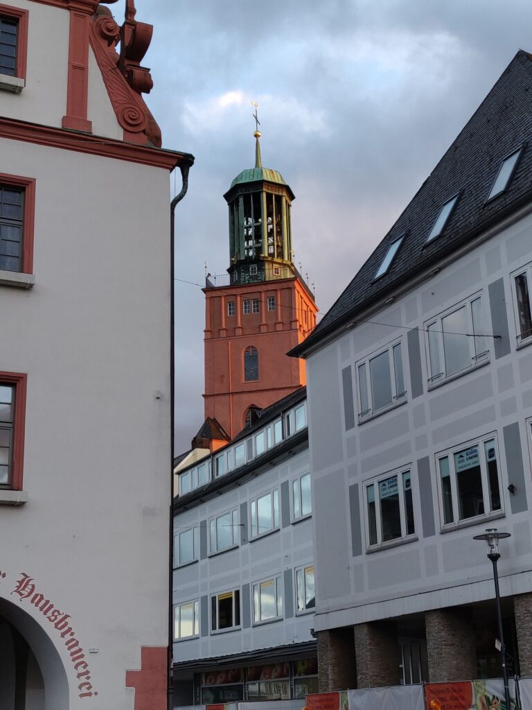 Roter und grüner Uhrturm über modernen und historischen Gebäuden - Symbol für würdevolle Bestattungen in Hessen.