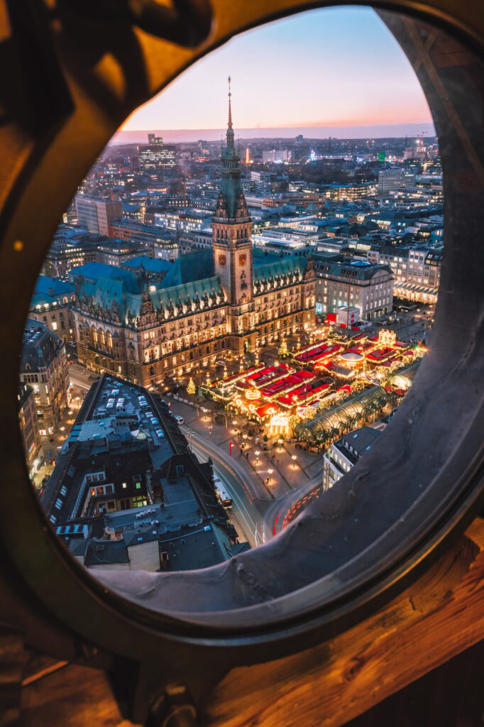 Blick durch ein rundes Fenster auf eine Stadt in der Dämmerung, symbolisch für würdige und bezahlbare Bestattungen in Hamburg.