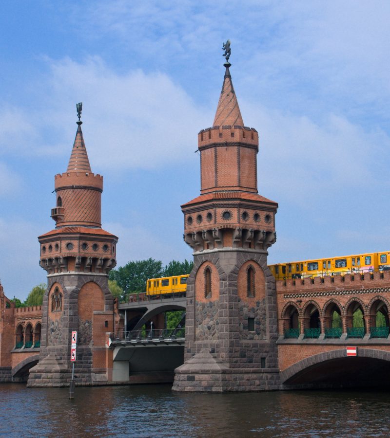 Gelber Zug fährt über die Oberbaumbrücke in Berlin - Symbol für Verlässlichkeit und Verbindungen deutschlandweiter Bestattungen.