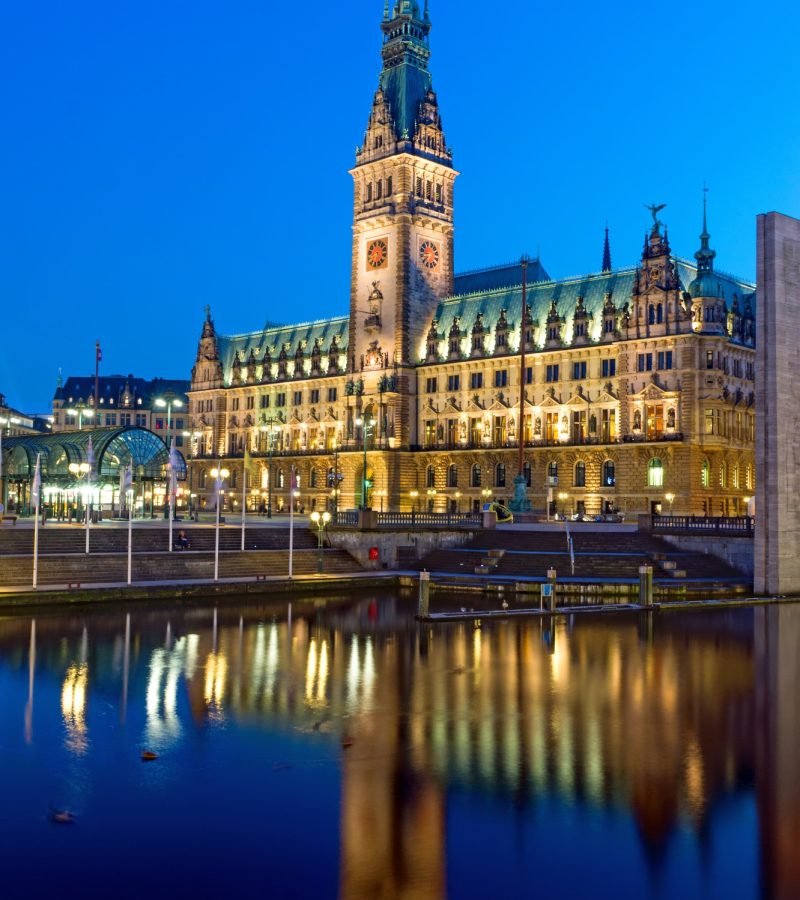 Hamburger Rathaus am Abend beleuchtet, spiegelt sich im Wasser - Symbol für würdevolle Bestattungen in ganz Deutschland.