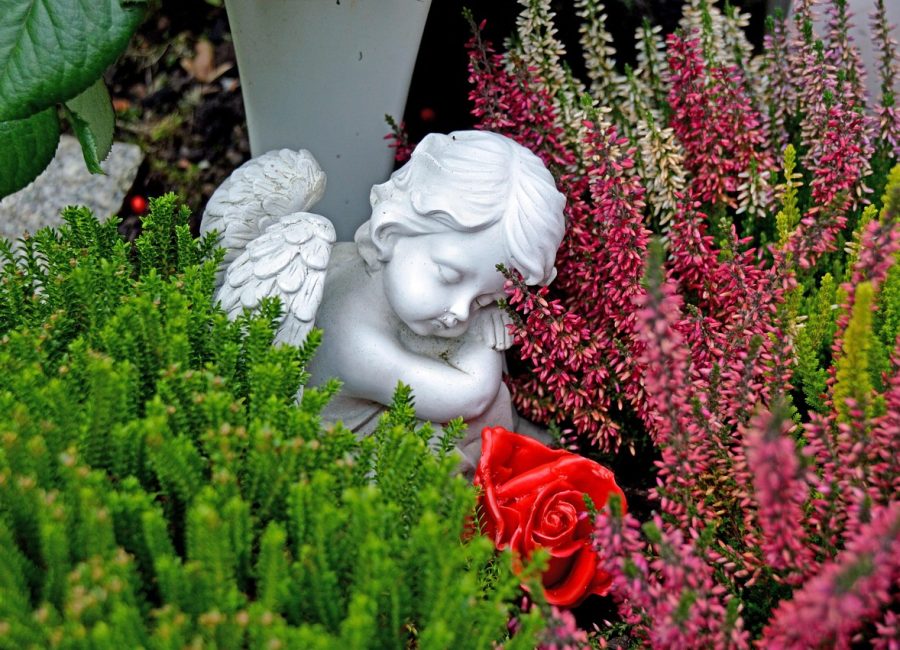 Weiße Engelsstatue zwischen Blumen und einer roten Rose - Symbol für würdevolle, preiswerte Bestattungen bei YANA.