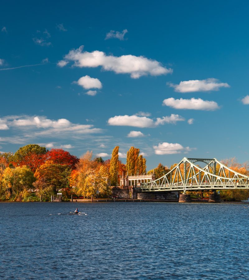 Herbstliche Flusslandschaft mit Brücke und Ruderboot - Symbol für einen würdevollen Abschied bei YANA Bestattungen.